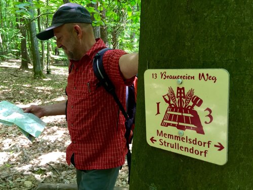 Wanderer der an einem Wegweiser des 13 Brauereien-Wegs lehnt und eine Karte studiert | © Tourismuszentrale Fränkische Toskana